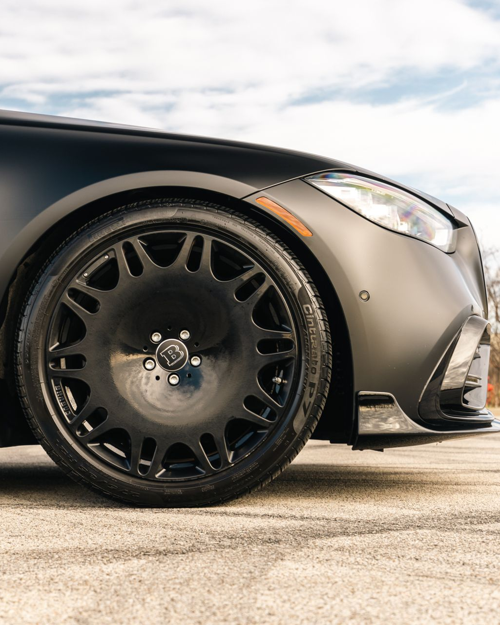 Close-up of a matte black sports car’s front wheel and bumper on pavement