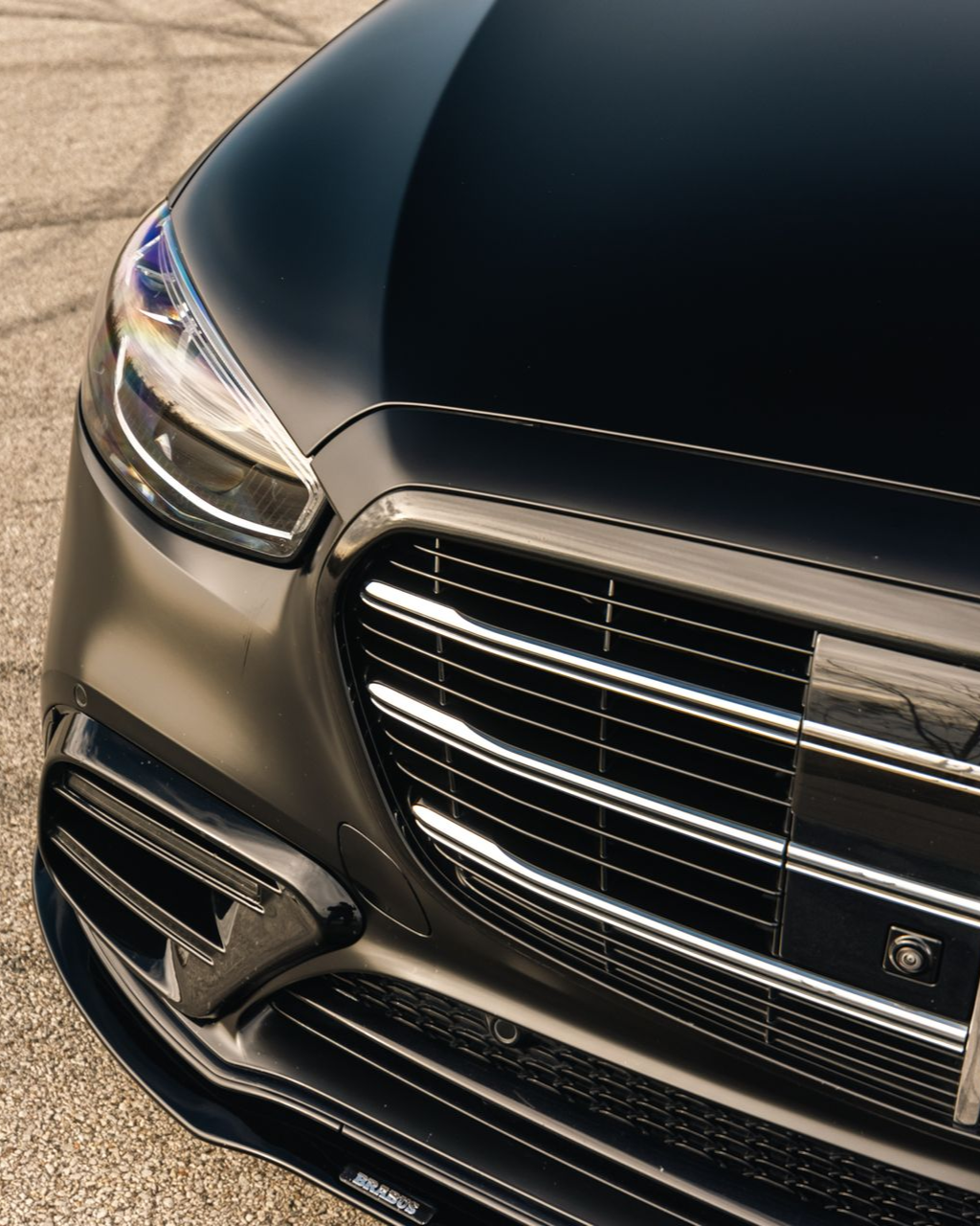 Close-up of a black luxury car’s front grille, headlight, and bumper outdoors.