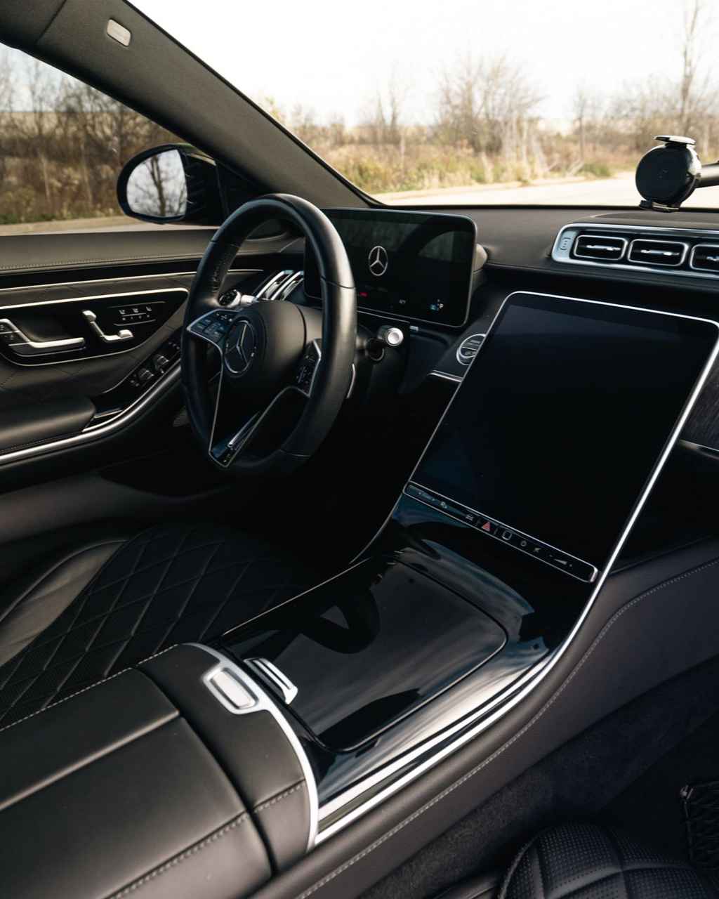 Luxury car interior with black leather seats, steering wheel, and large center touchscreen.