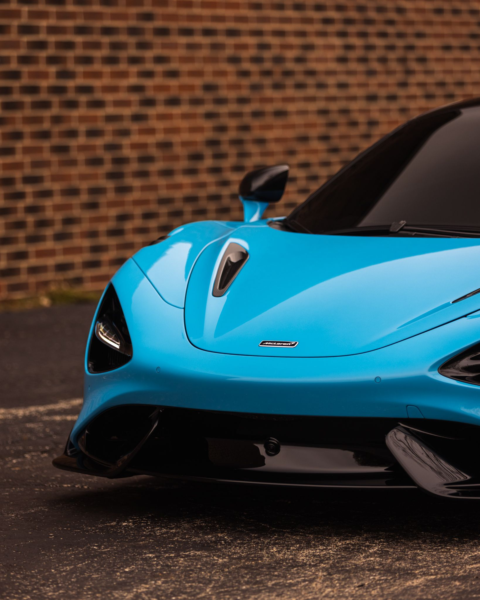 Bright blue sports car front end parked against a brick wall