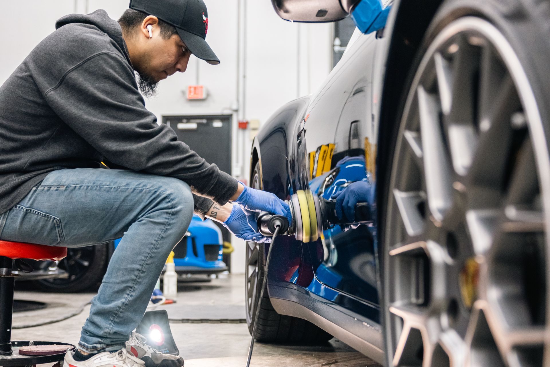 Mechanic buffing a blue sports car’s side panel in an auto shop