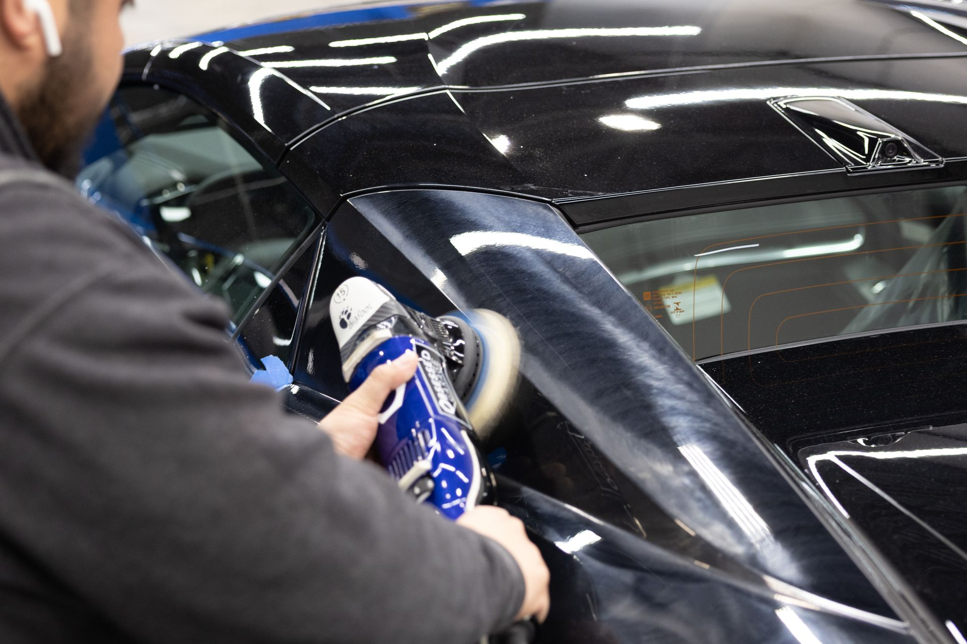 Person polishing a black car with a blue buffer in a garage