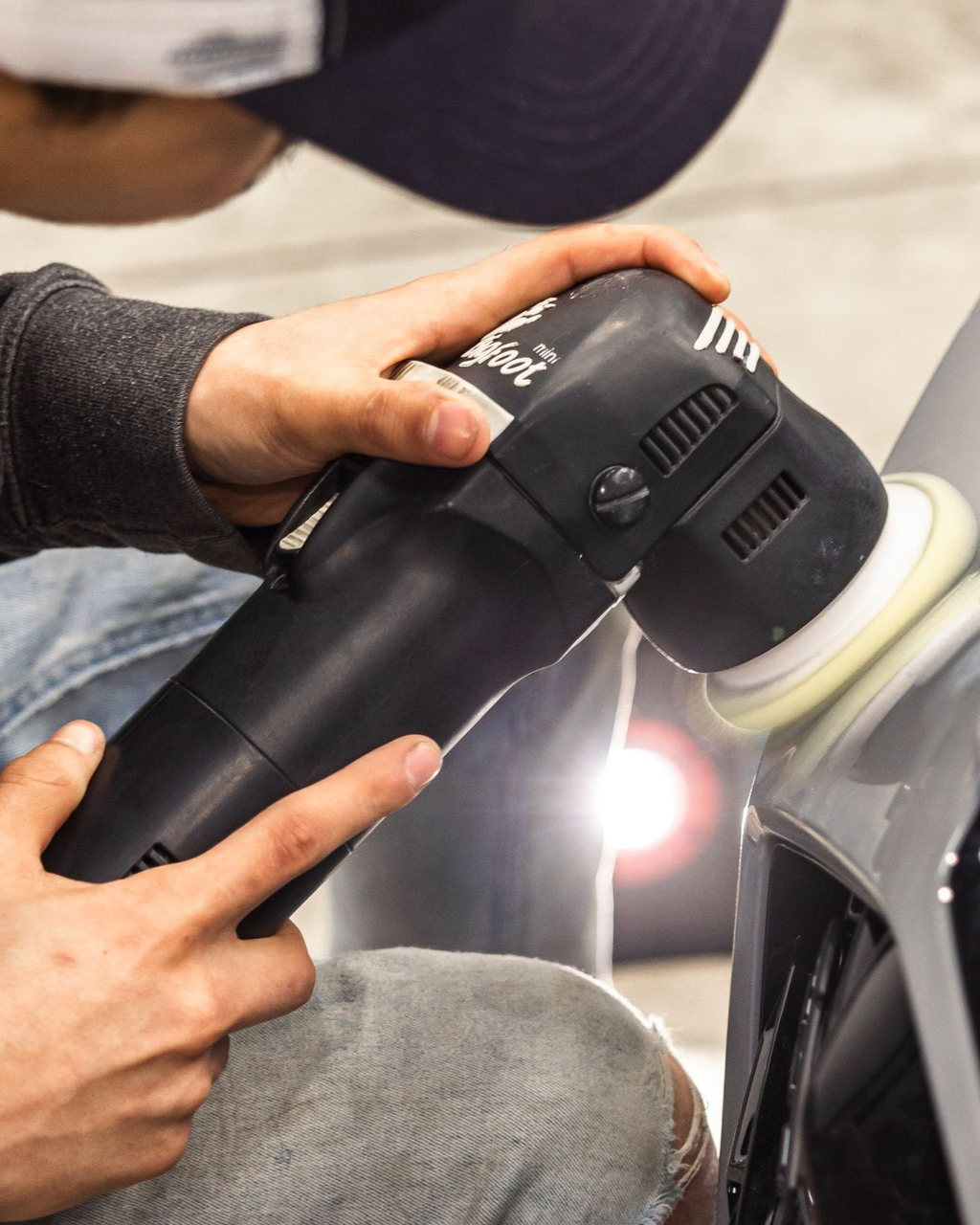 Person using a black handheld polisher on a car panel, buffing the surface