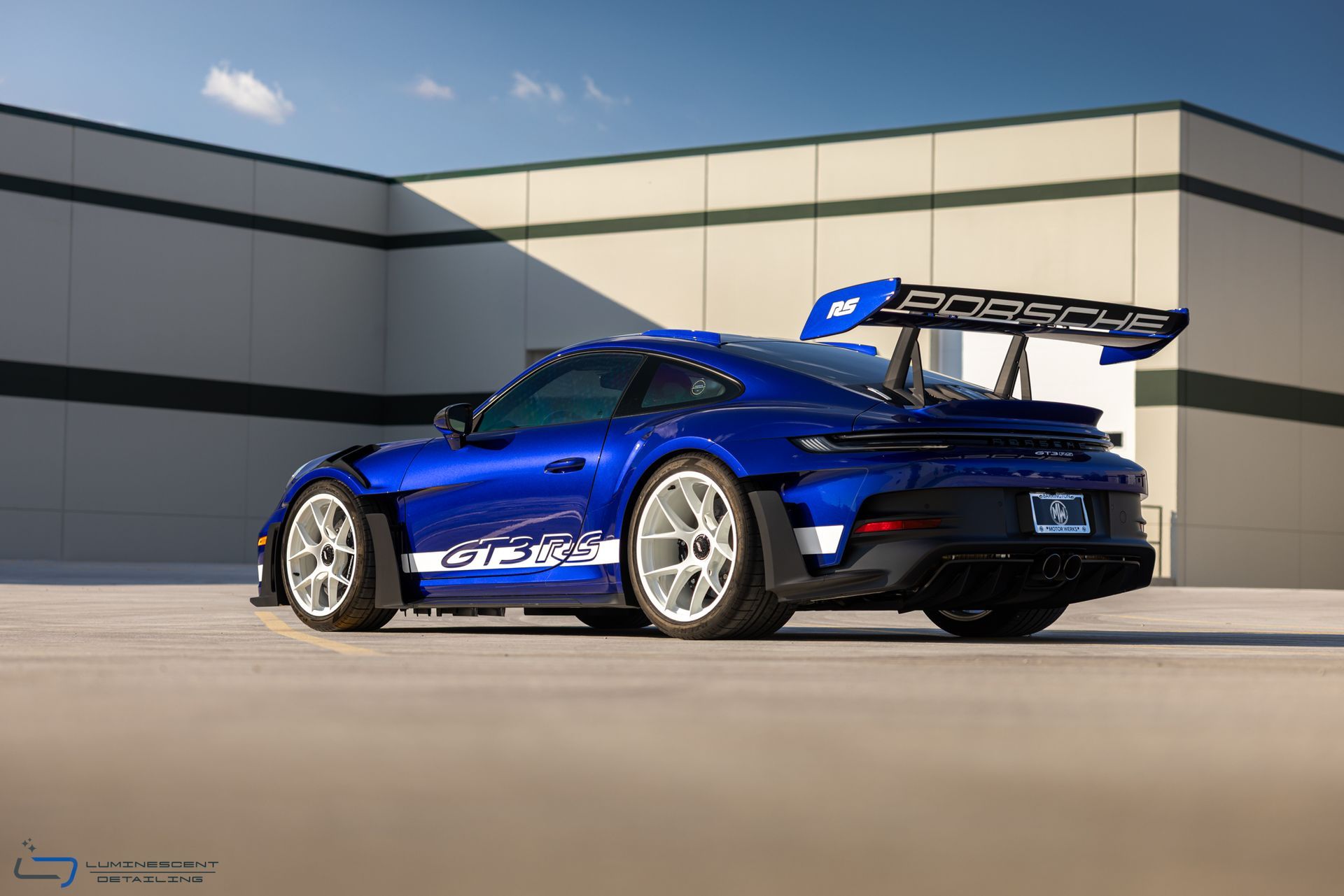 Blue sports car with large rear wing parked beside a modern building