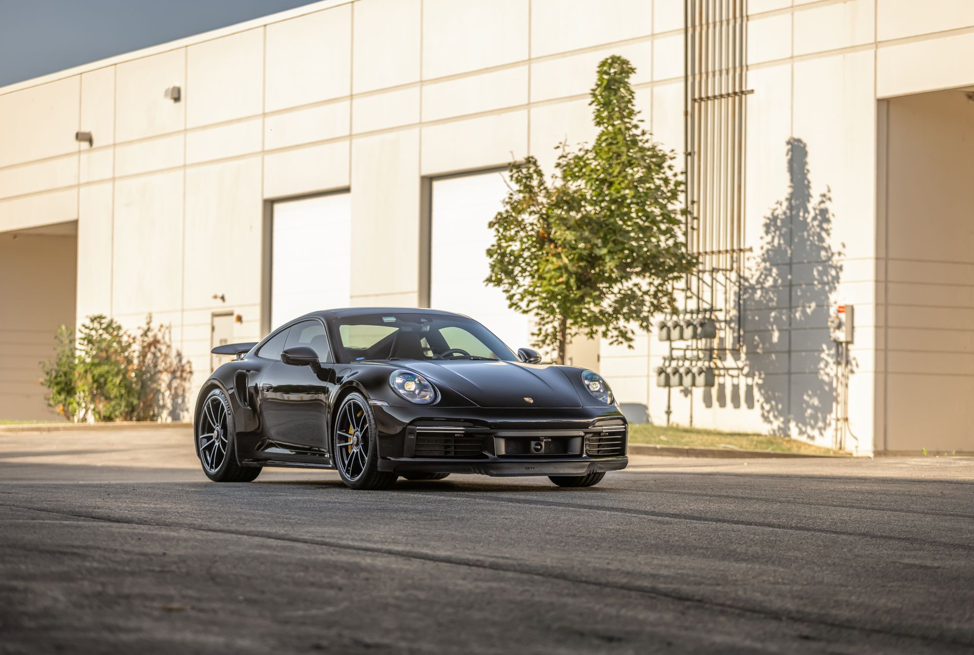 Black sports car parked in front of a white industrial building