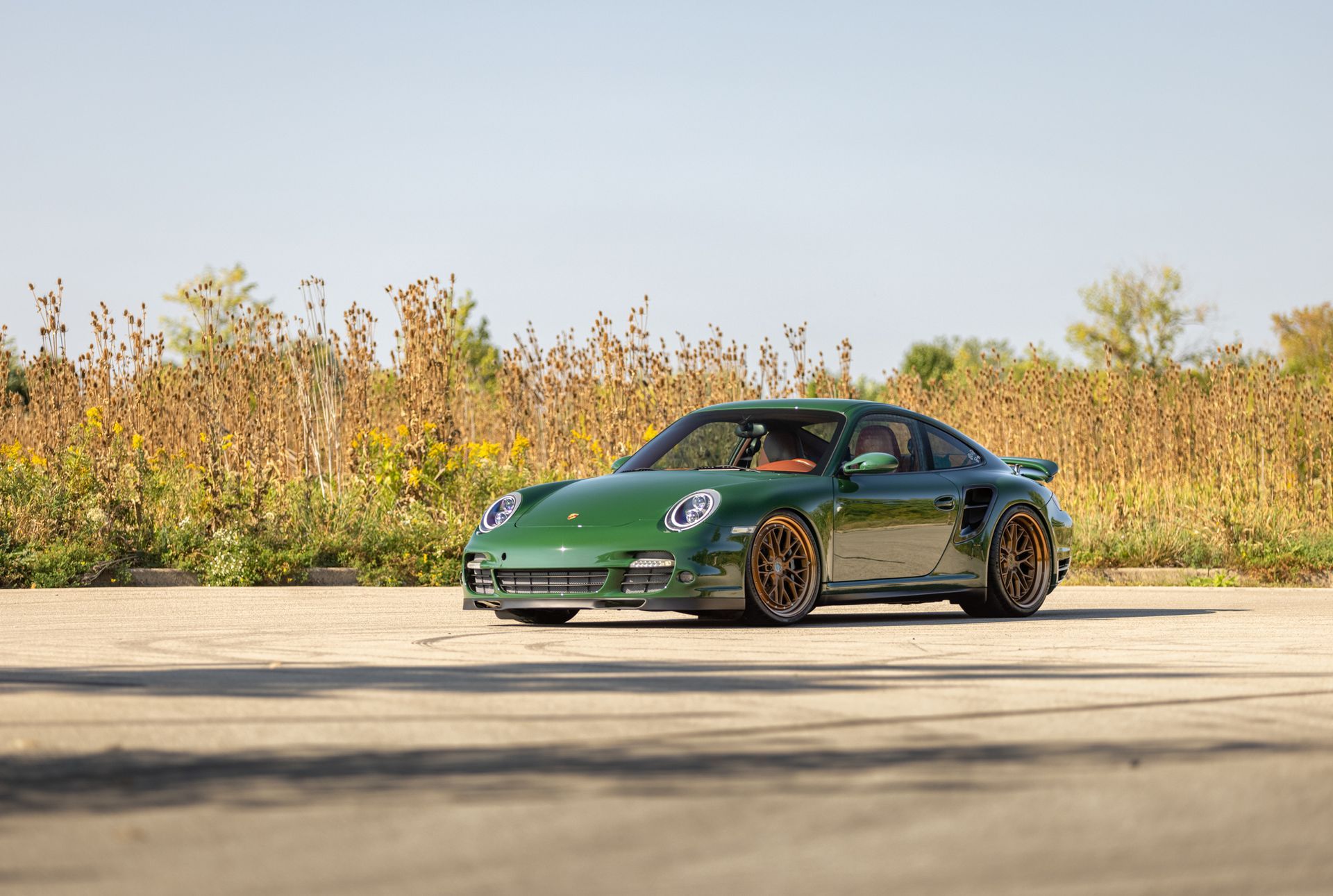 Green sports car parked on a concrete lot with autumn trees in the background