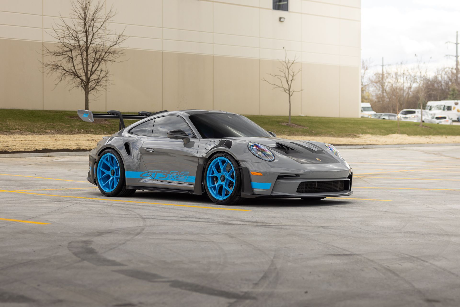 Gray sports car with bright blue wheels parked in a lot beside a beige building
