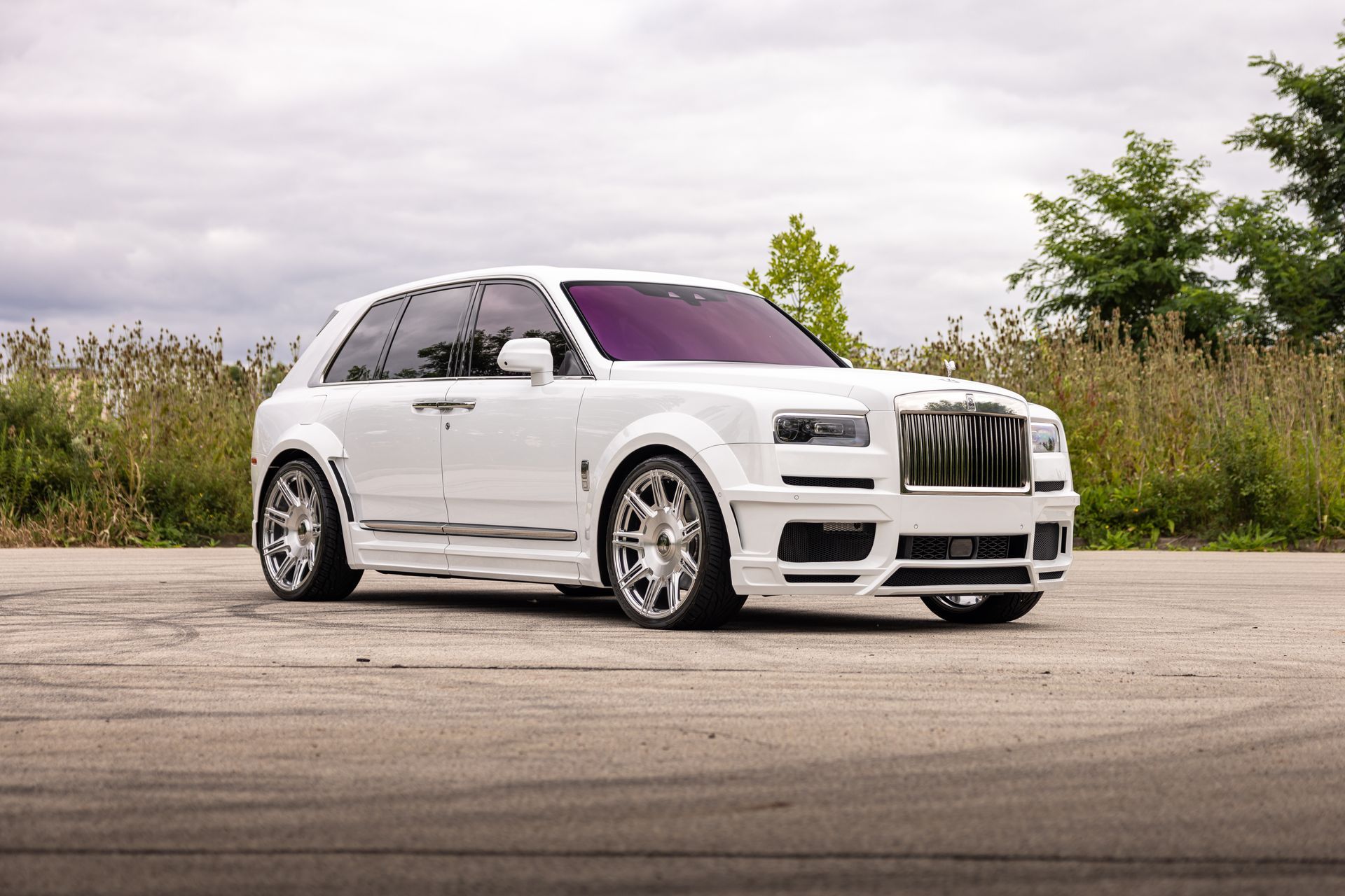 White SUV parked on pavement with tinted windows, chrome wheels, and a purple-tinted windshield in an outdoor setting