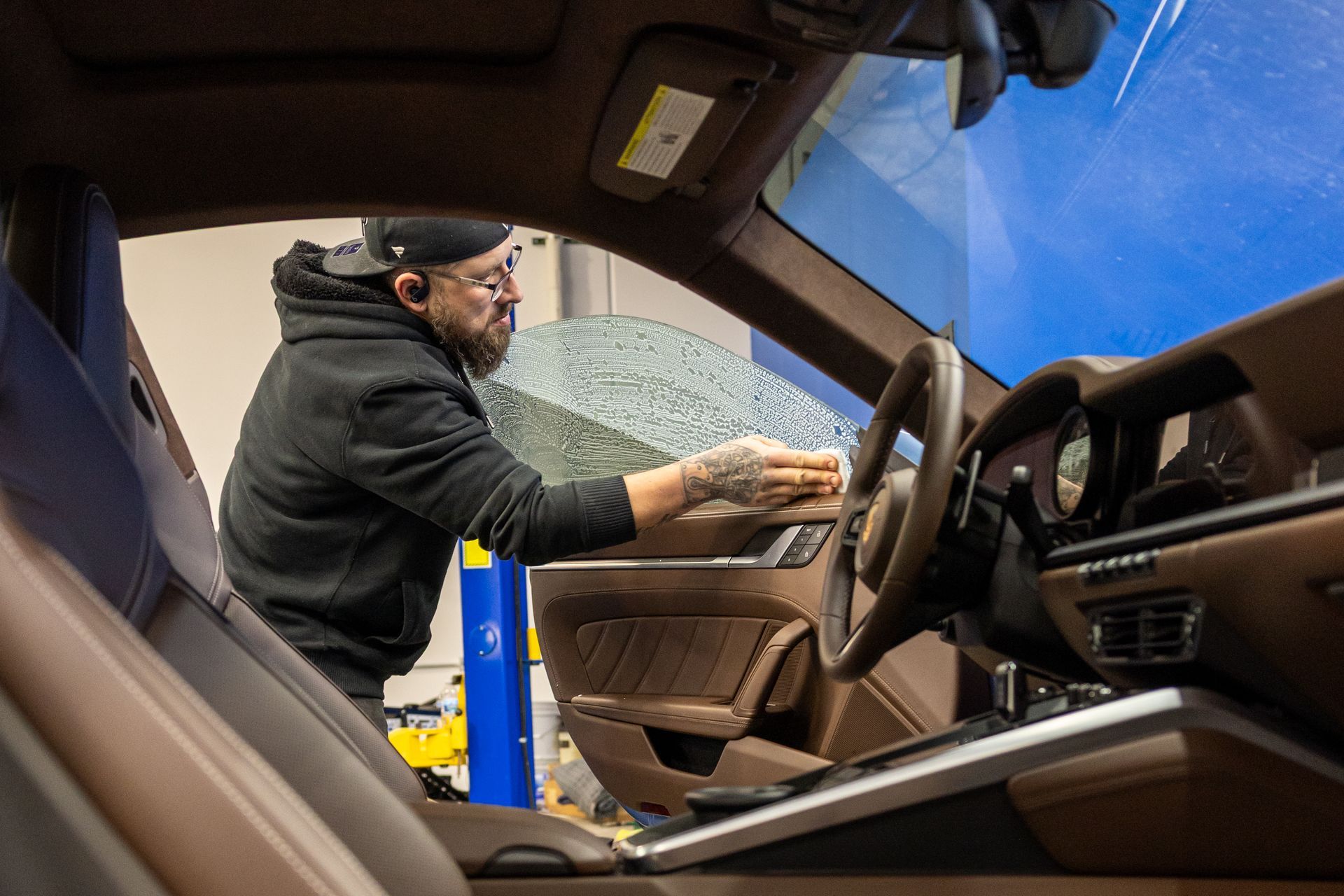Man cleaning shattered glass inside a car near the steering wheel and dashboard
