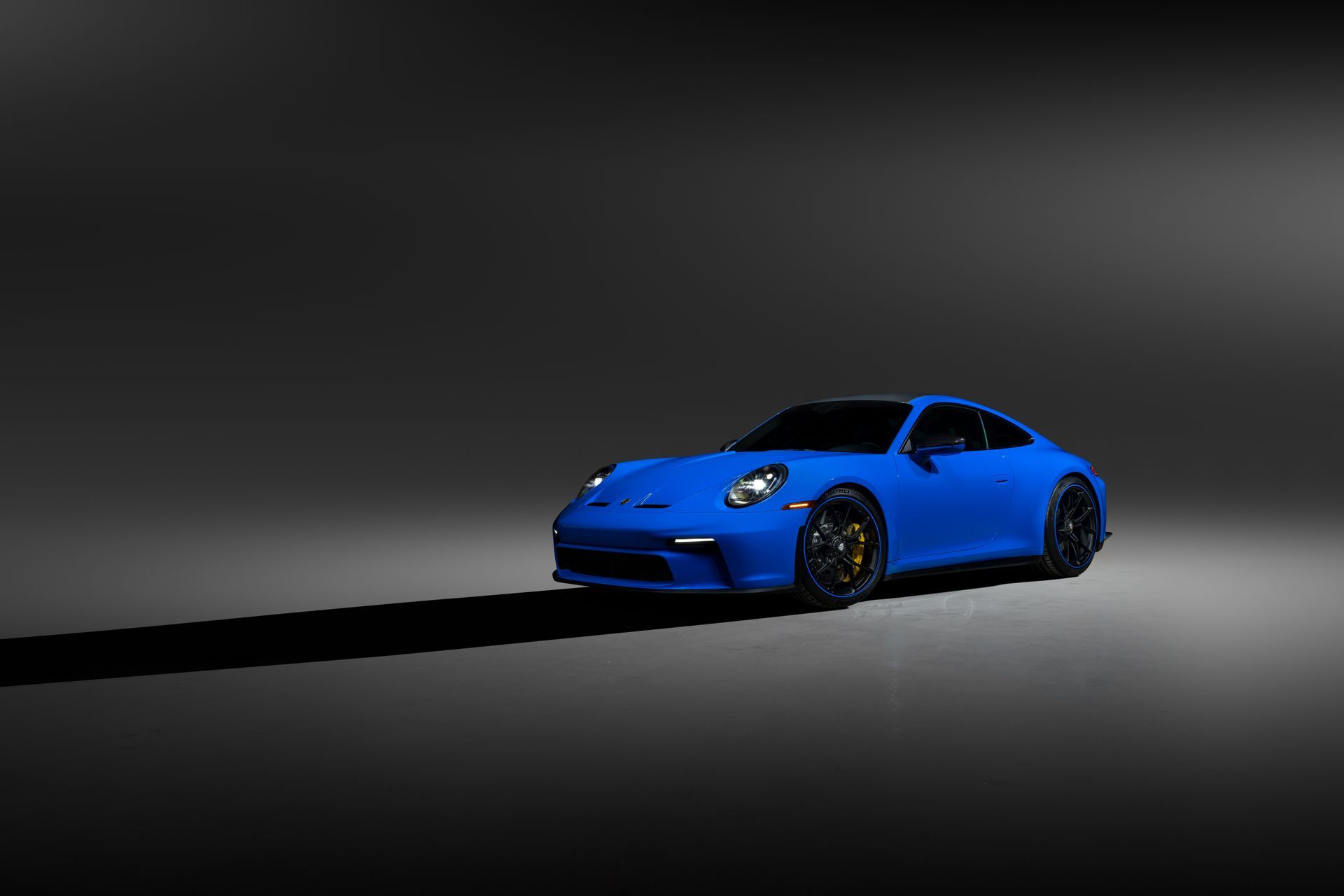 Blue sports car on a dark studio background, lit with a spotlight and long shadow.