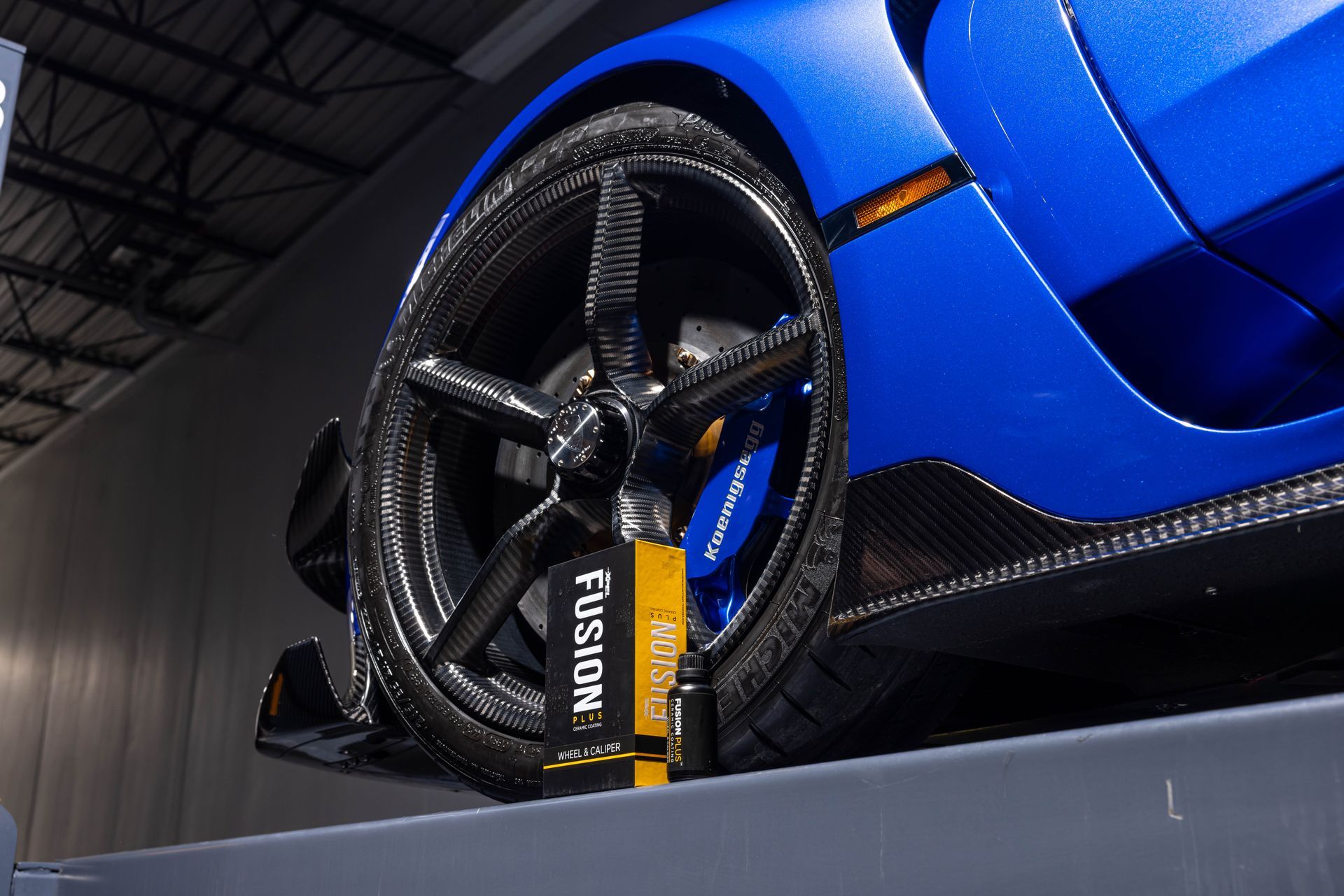Blue sports car close-up showing black alloy wheel and tire on a display stand.