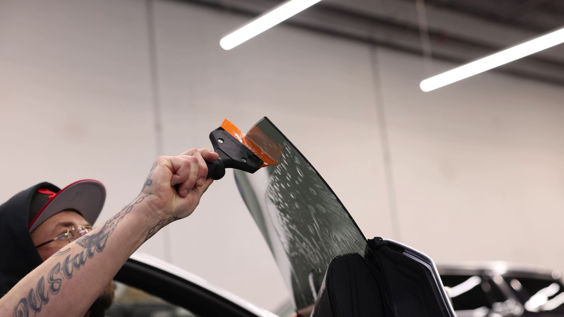 Person using a scraper to remove film from a car windshield in a workshop
