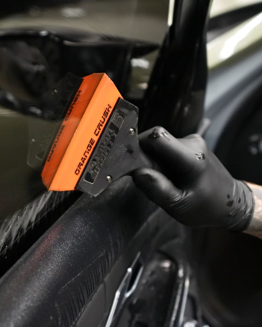 Close-up of a hand holding an orange squeegee against a car window film during installation