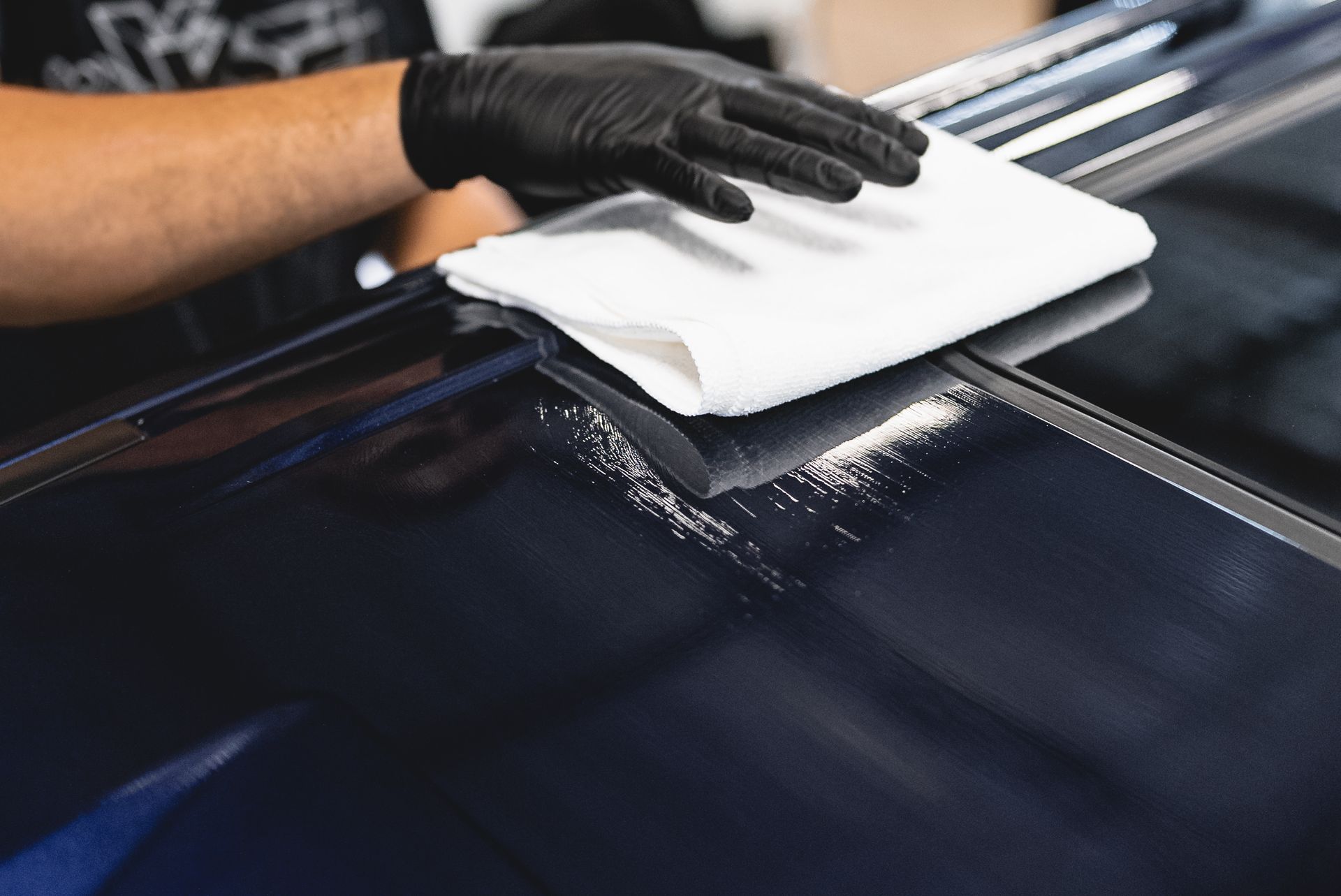 Gloved hand wiping a glossy dark car hood with a white cloth