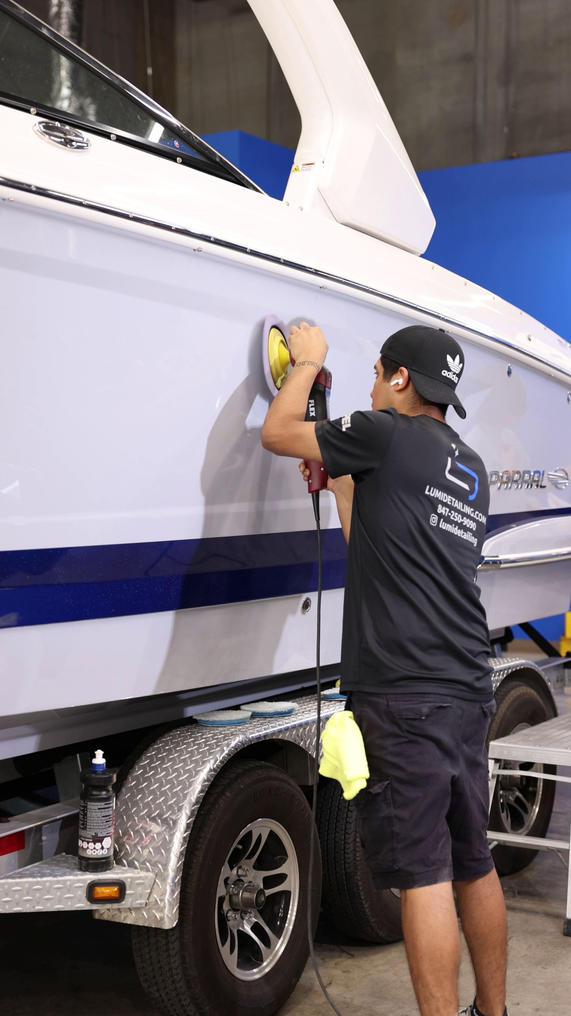 Person polishing the side of a white boat on a trailer in a workshop, using a yellow cloth.