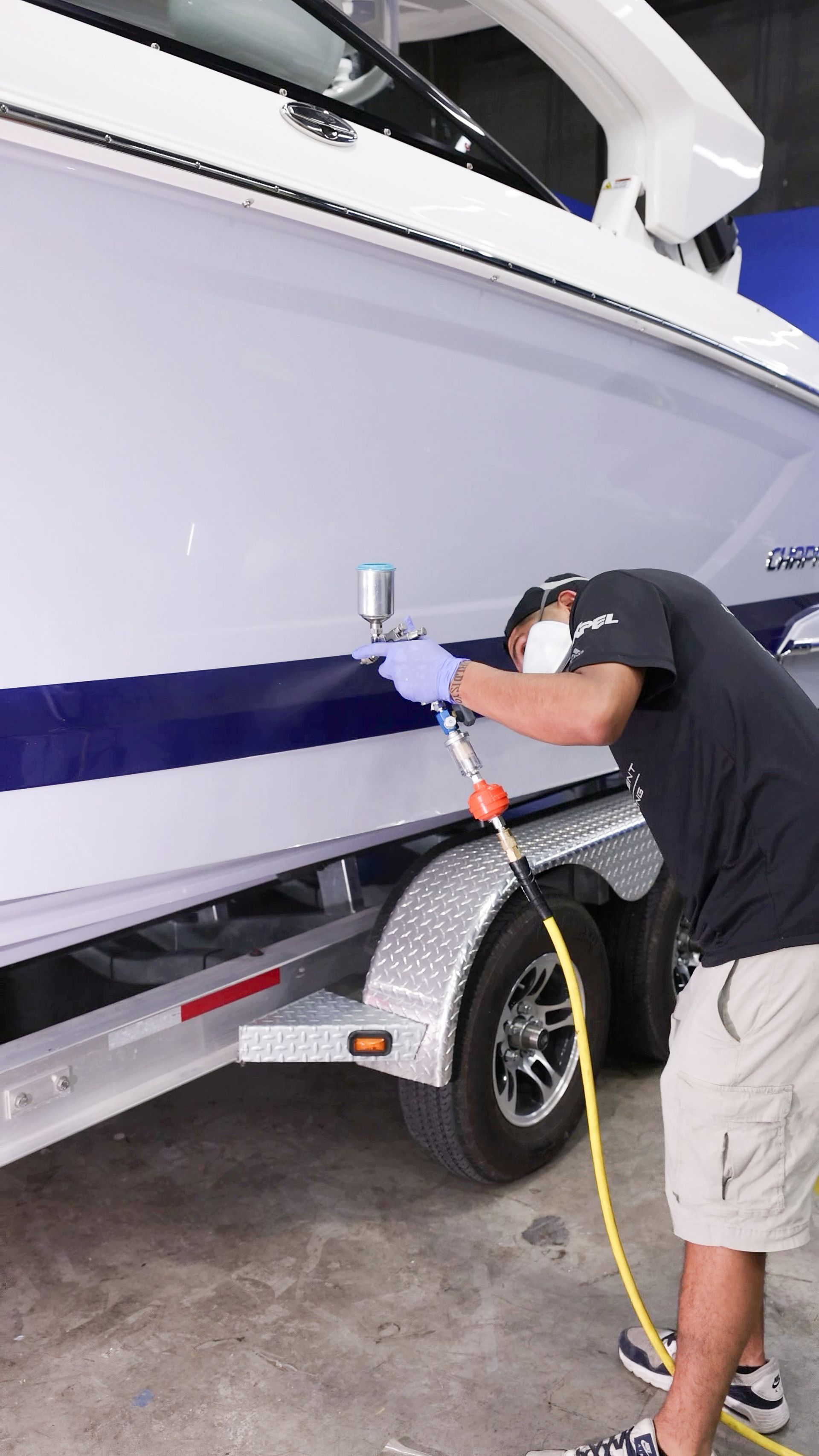 Man pressure-washes a white boat on a trailer with a yellow hose in a garage