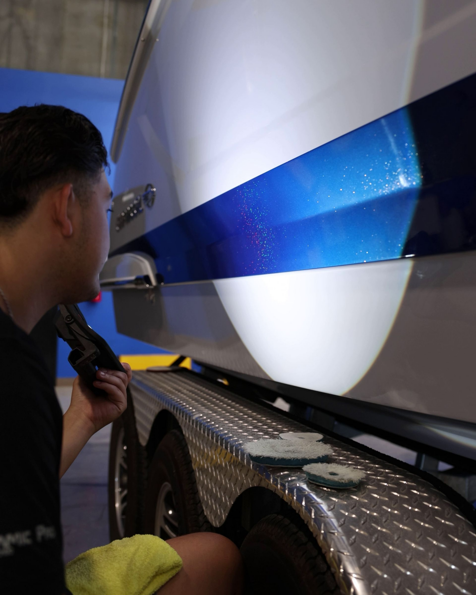 Person inspecting a large white vehicle with a blue stripe beside a diamond-plate trailer