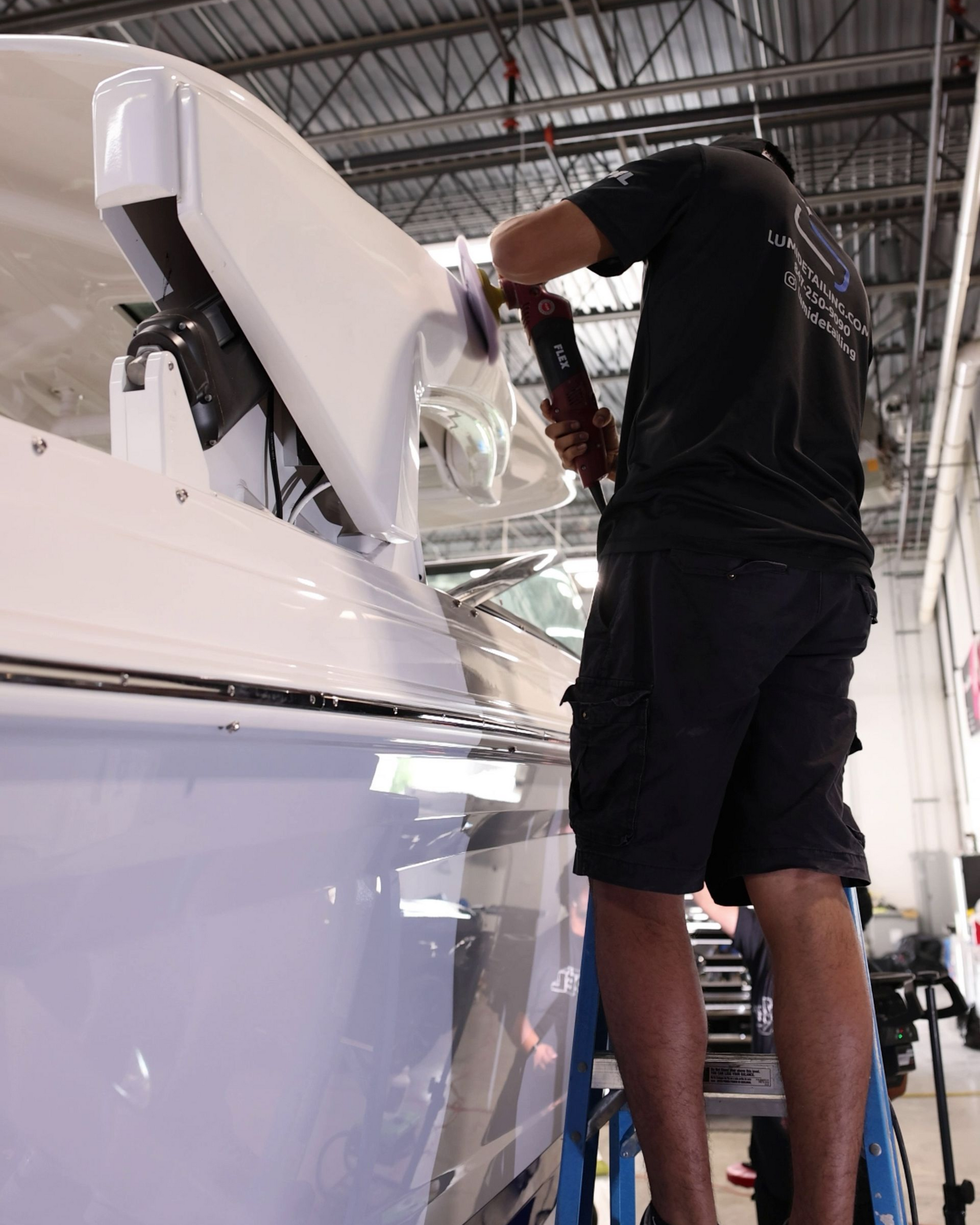 Person polishing a white boat hull in a workshop, reaching into the open compartment.