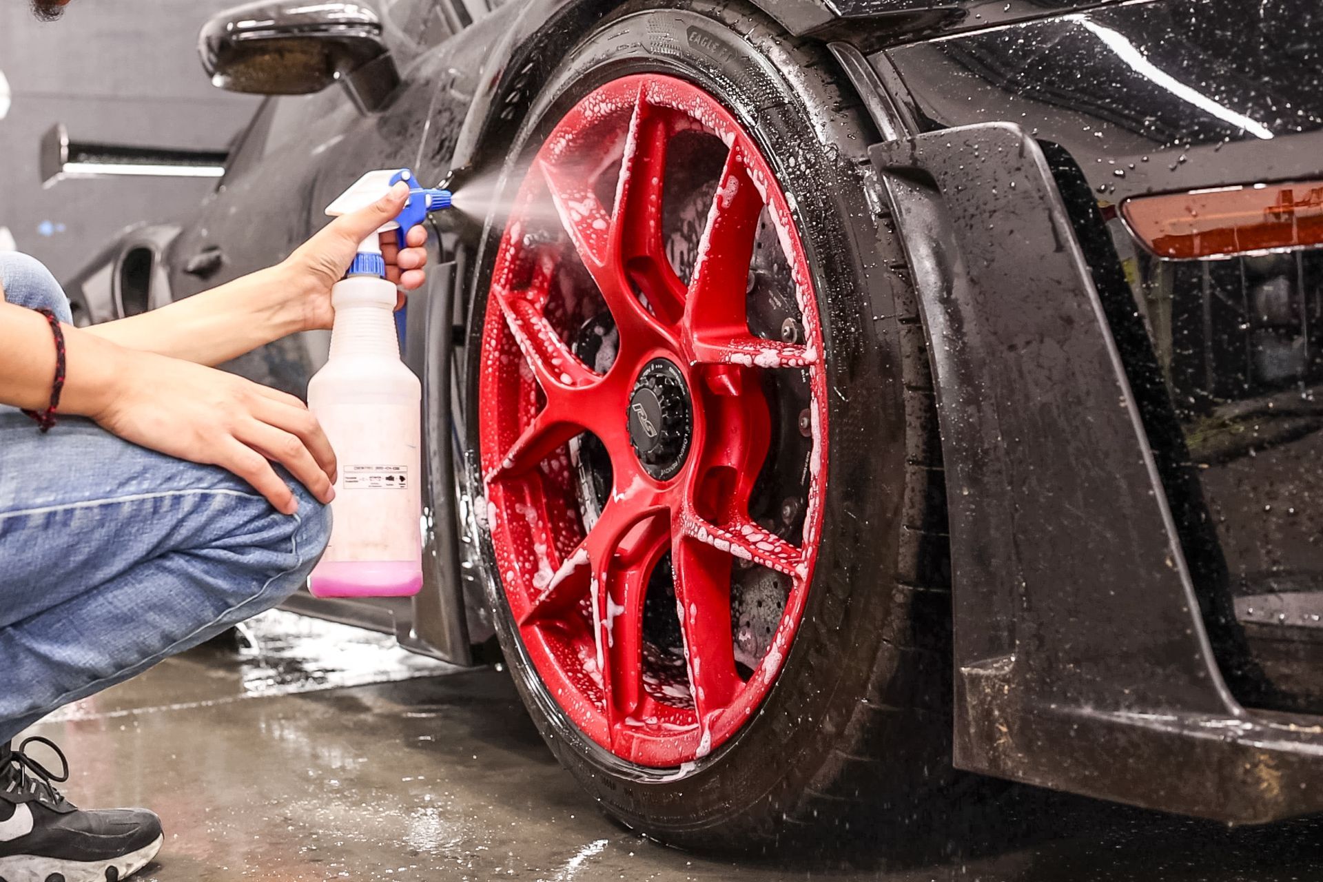 Person sprays cleaner on a red car wheel during a car wash