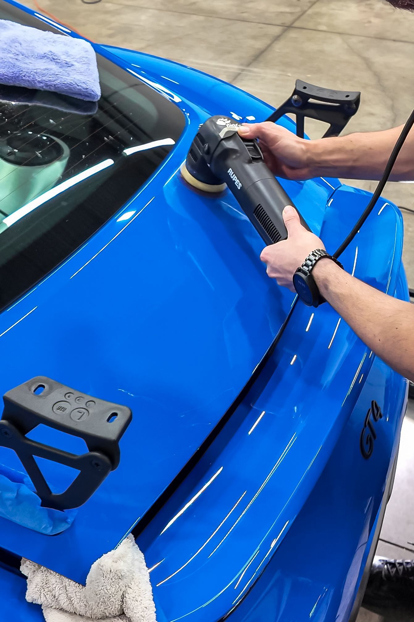 Worker in a blue cap sanding an orange vehicle panel in a workshop
