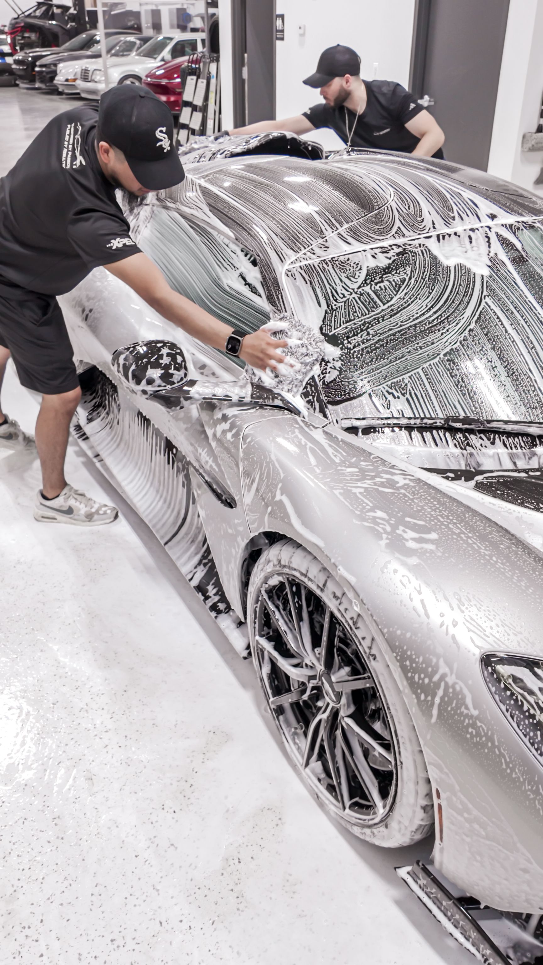 Red car being sprayed with a hose and soap during a car wash, close-up of rear wheel and side panel