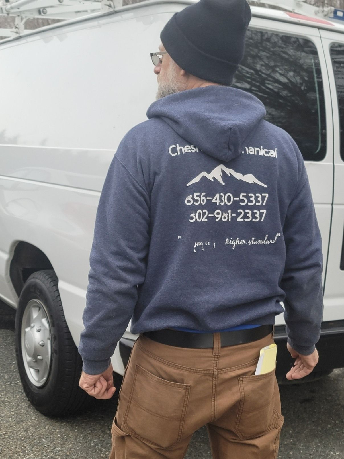 A person stands with their back to the camera, wearing a dark blue hoodie with a white mountain logo and phone numbers.