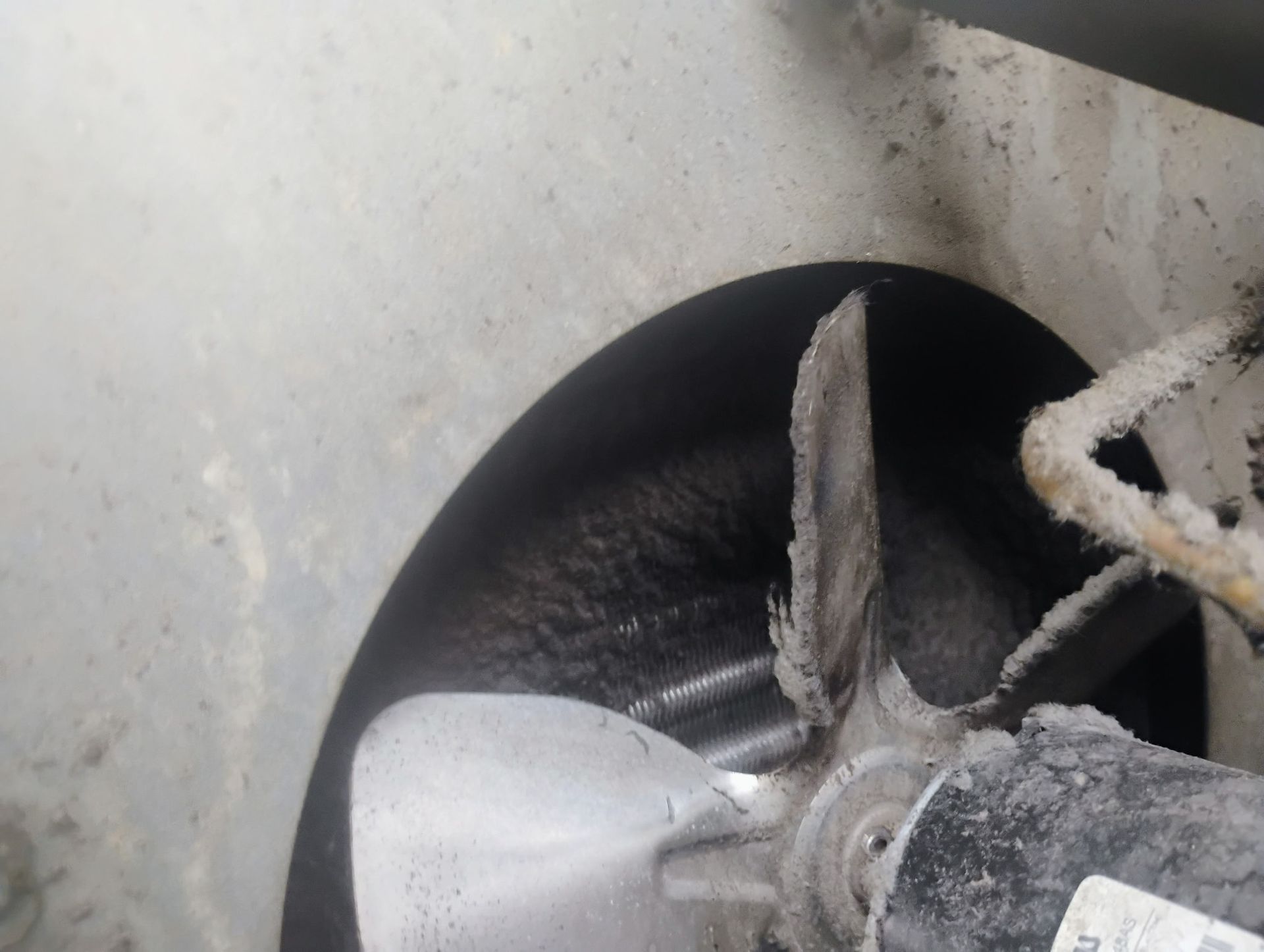 A dirty, three-blade metal fan inside a metallic housing, covered in layers of thick, dark dust and grime.