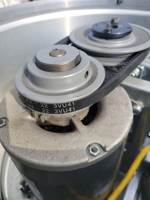 A close-up view of an electric motor shaft with a black belt connected to a pulley system.