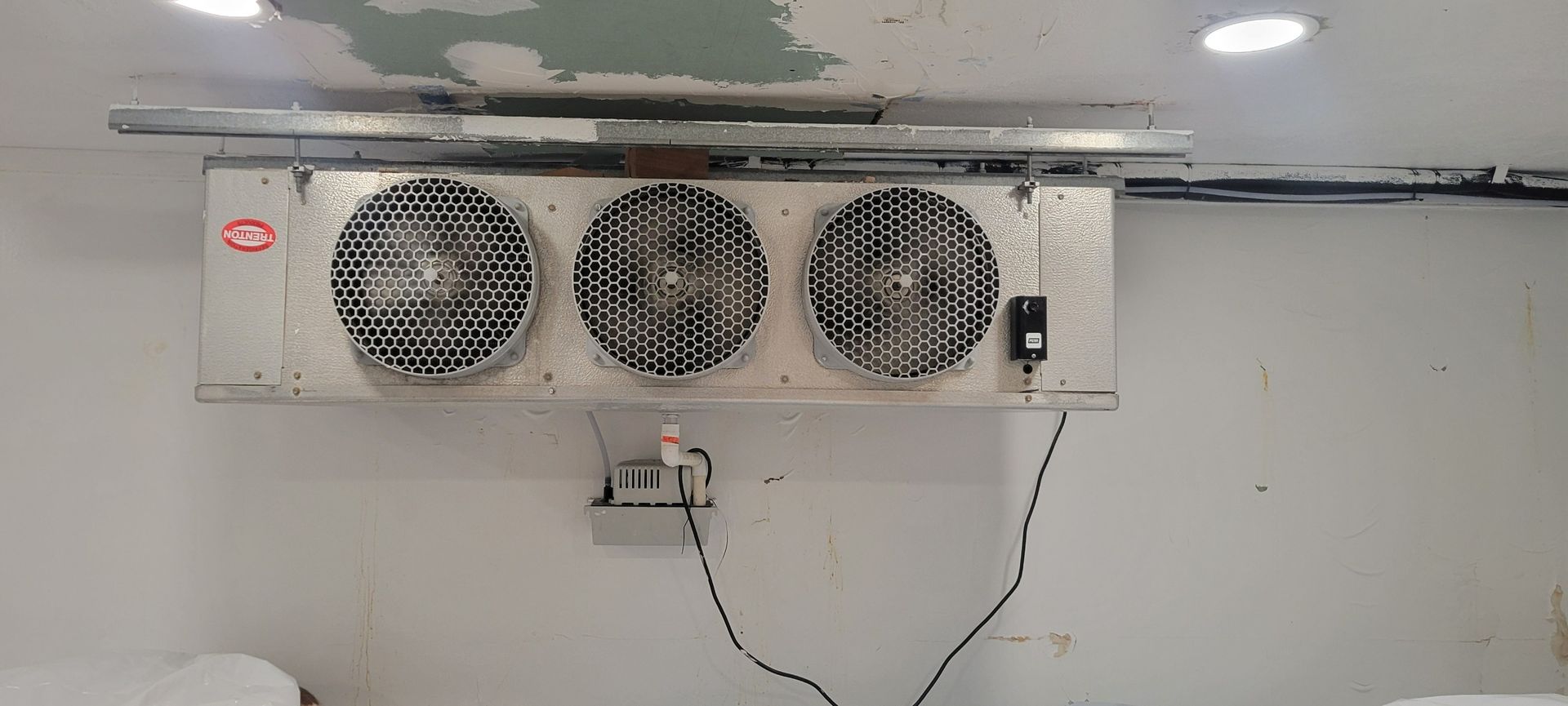 An industrial triple-fan ceiling-mounted cooling unit installed against a white wall.