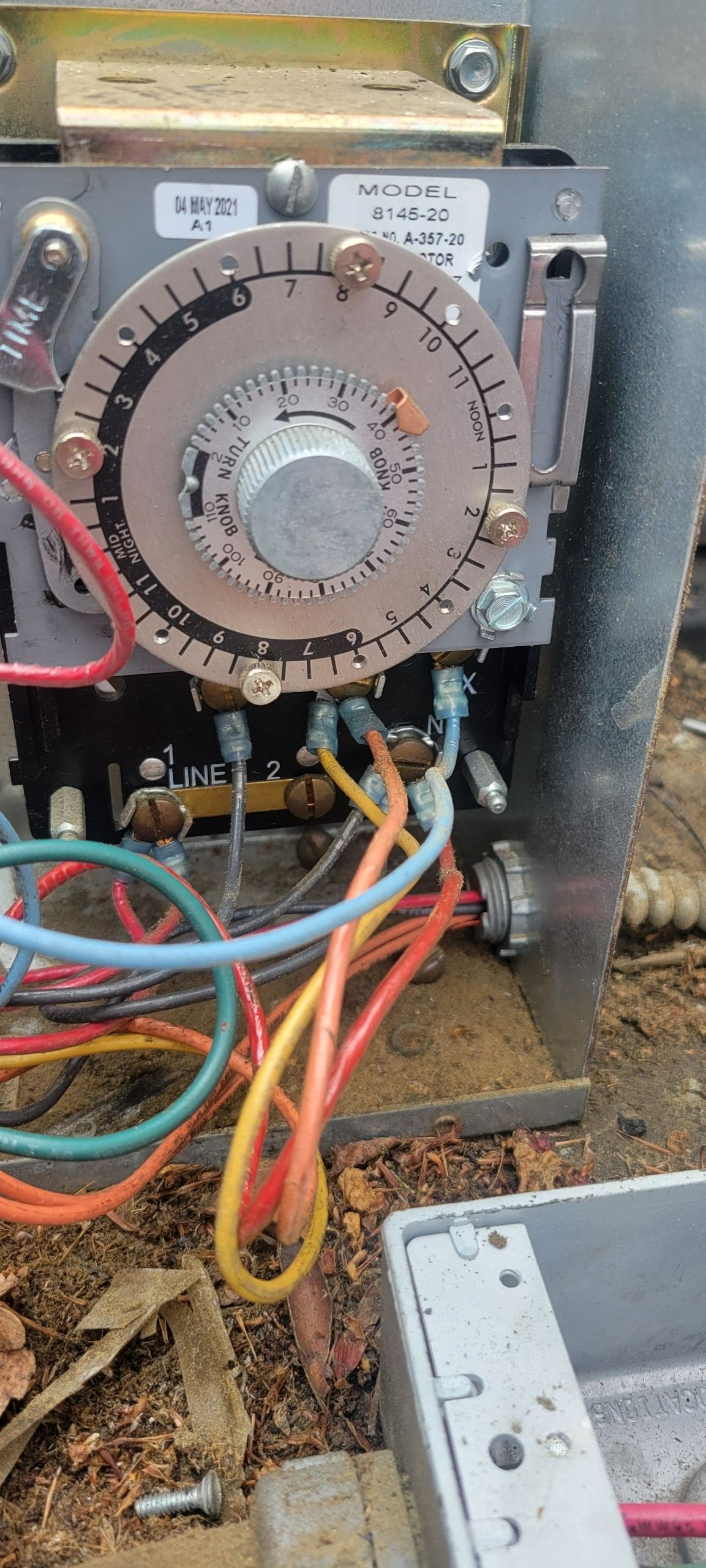 An industrial electrical timer switch with a circular dial and multiple colored wires, mounted inside a metal box.