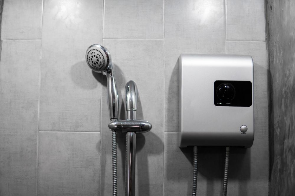 A wall-mounted showerhead on a slide bar next to a silver electric water heater against a tiled bathroom wall.