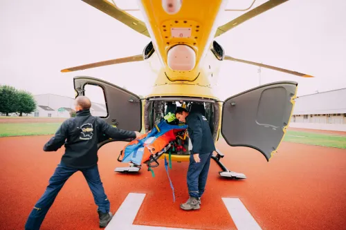 People unloading a person on a stretcher from a yellow helicopter on a red helipad
