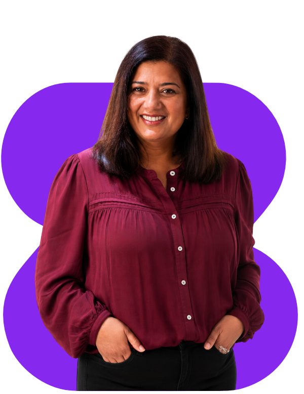 Smiling woman in burgundy blouse with hands in pockets, standing before a purple abstract background.