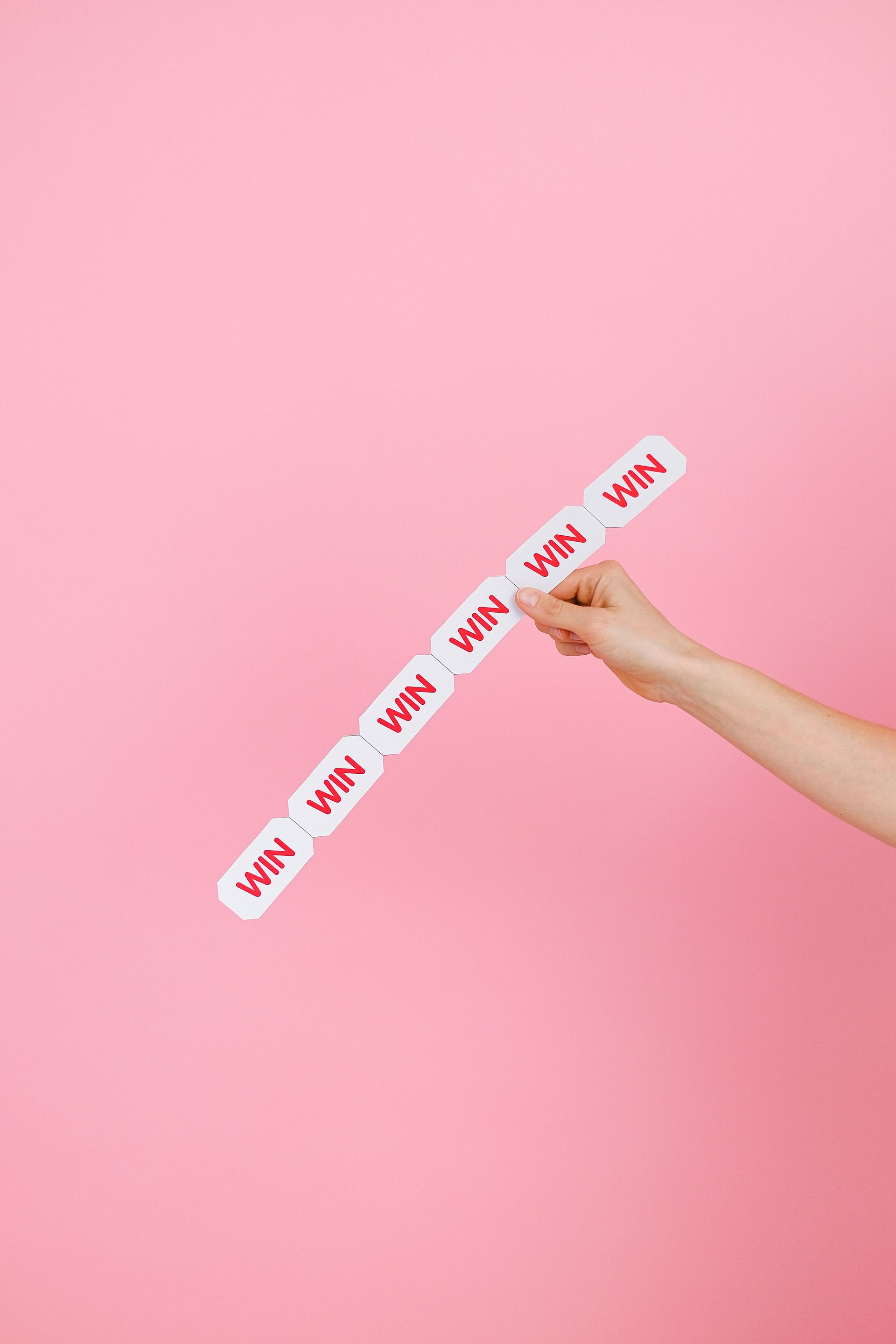 Hand holding a strip of repeated pink “why” labels on a pink background