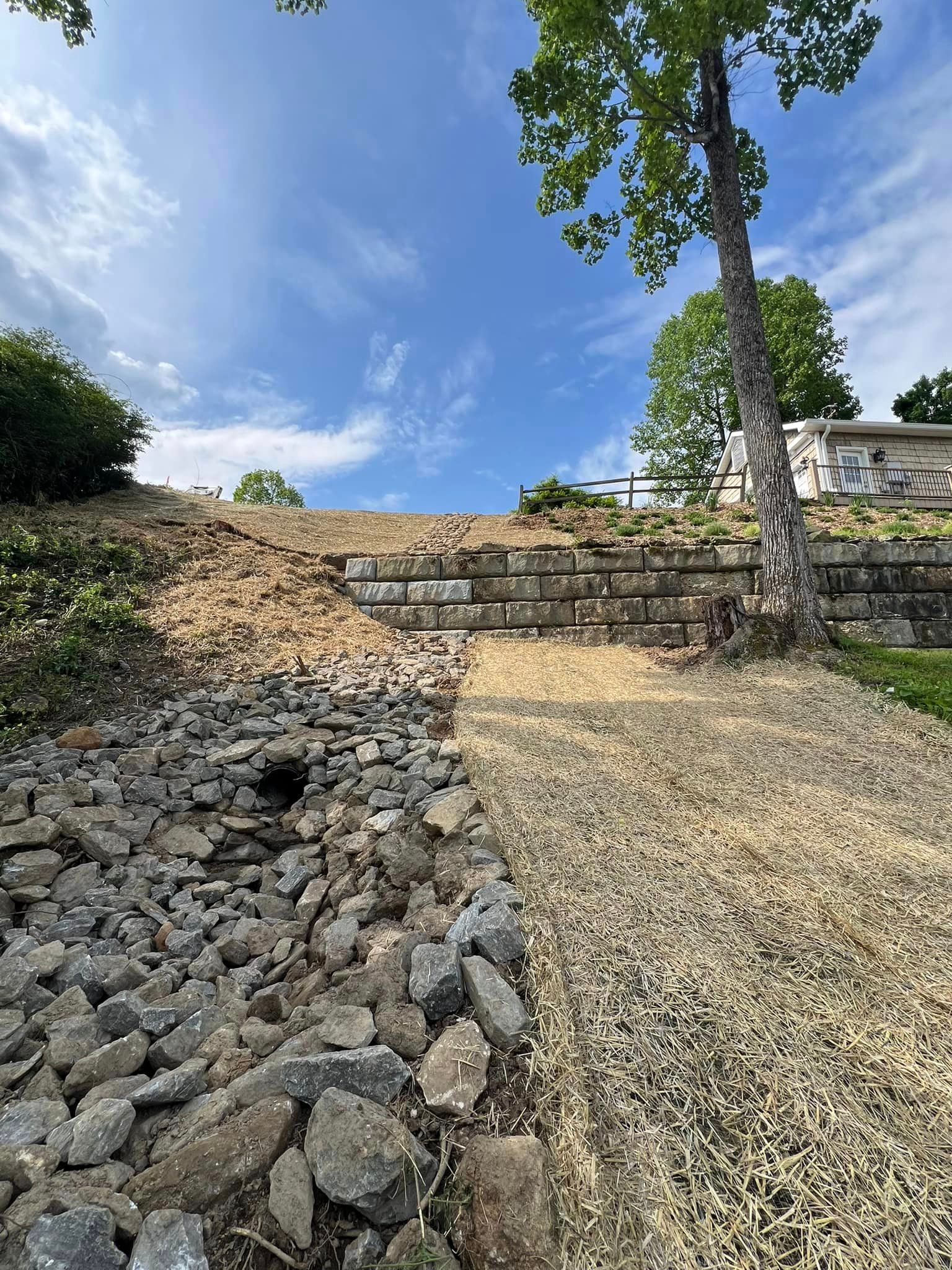A gravel path leading up to a stone wall with a tree in the background.