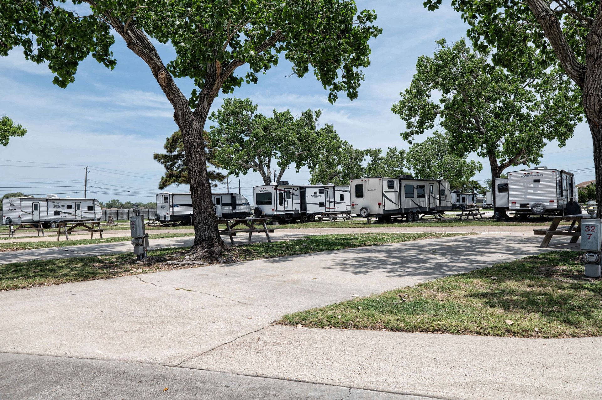 RVs parked at a grassy campground under large trees on a sunny day