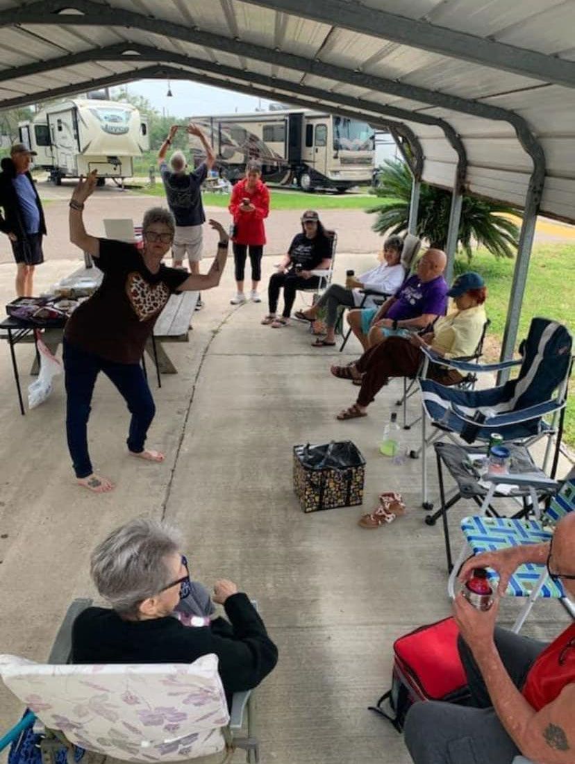 People seated in folding chairs under a canopy, with one woman dancing in the foreground.