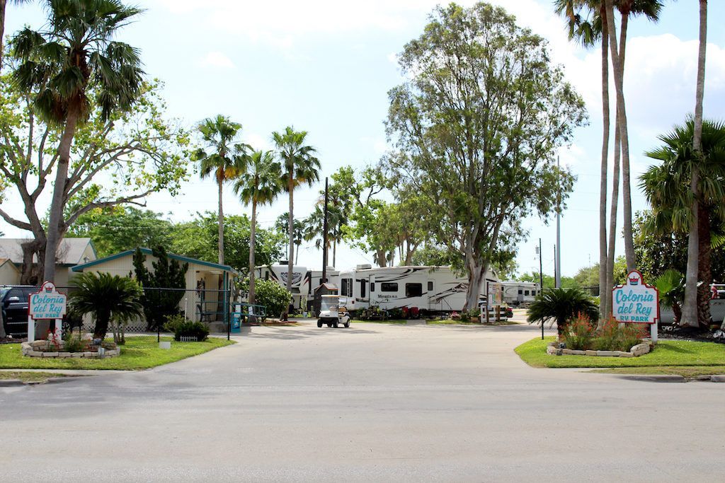 Entrance road to a campsite with trees, signs, and parked RVs in the distance.