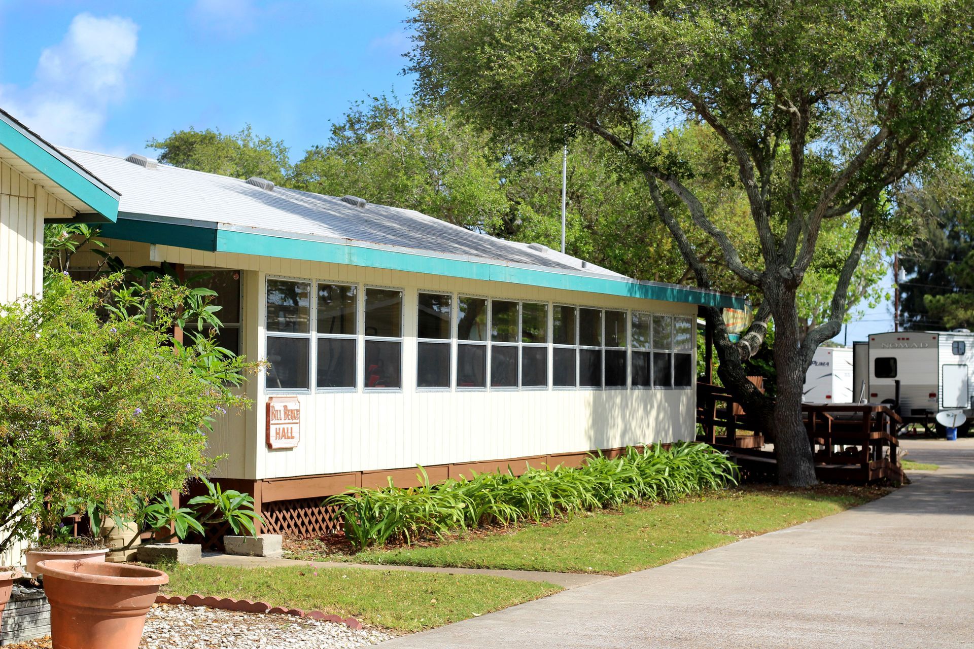 Small white building with teal roof beside a tree-lined driveway on a sunny day