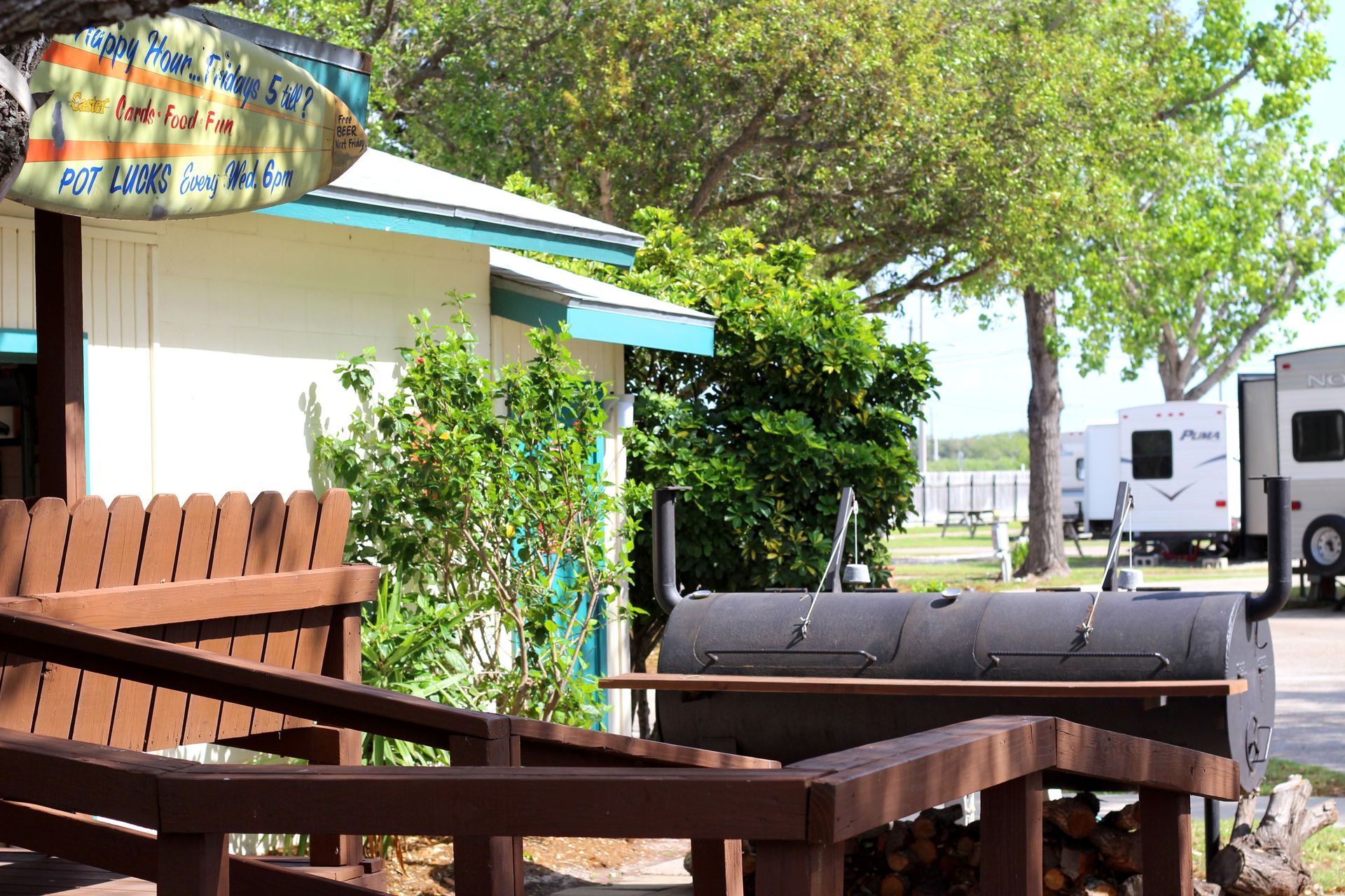 Outdoor patio with wooden picnic tables, a grill, and RVs parked beside a small building under trees
