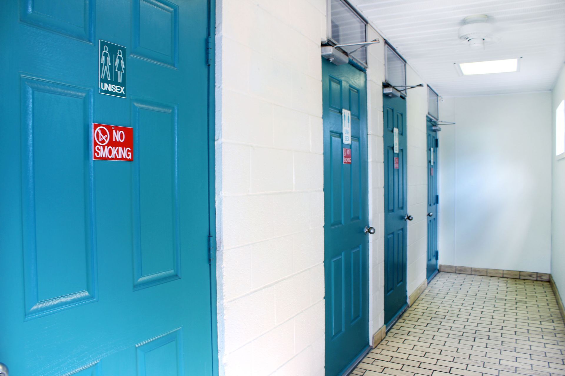 Blue restroom doors in a white hallway with tiled floor