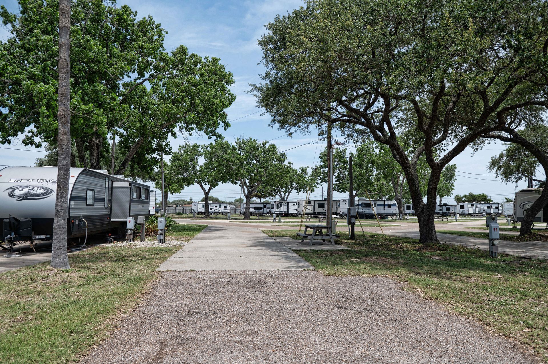 Gravel path through a tree-lined RV park with parked trailers and grassy areas on both sides