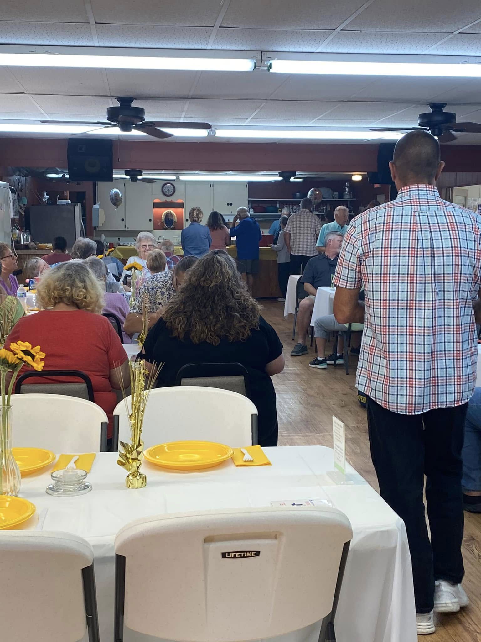 Banquet hall with seated guests, yellow plates on tables, and a man standing near the aisle
