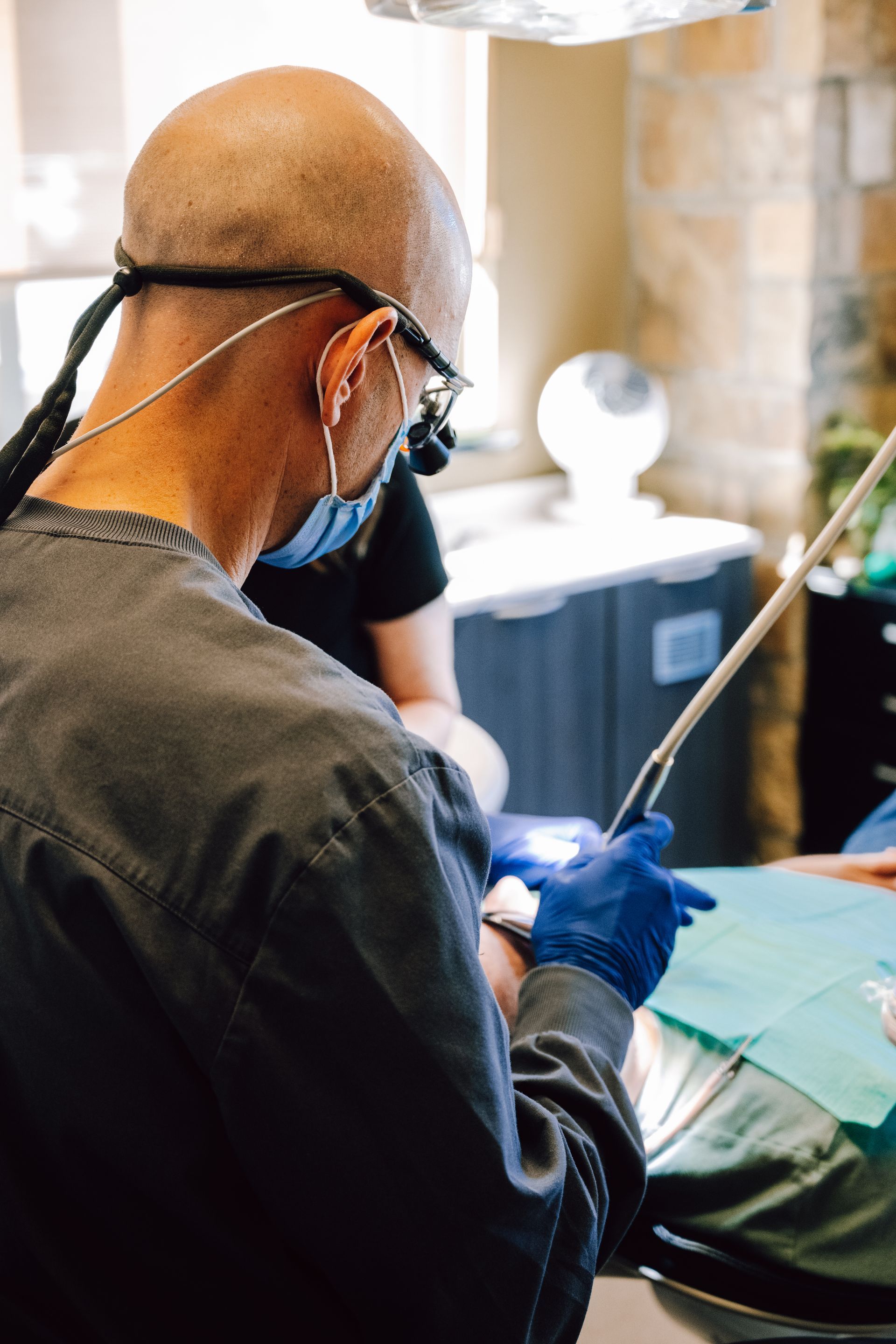 Dentist performing procedure on patient; blue gloves, mask, and surgical tools.