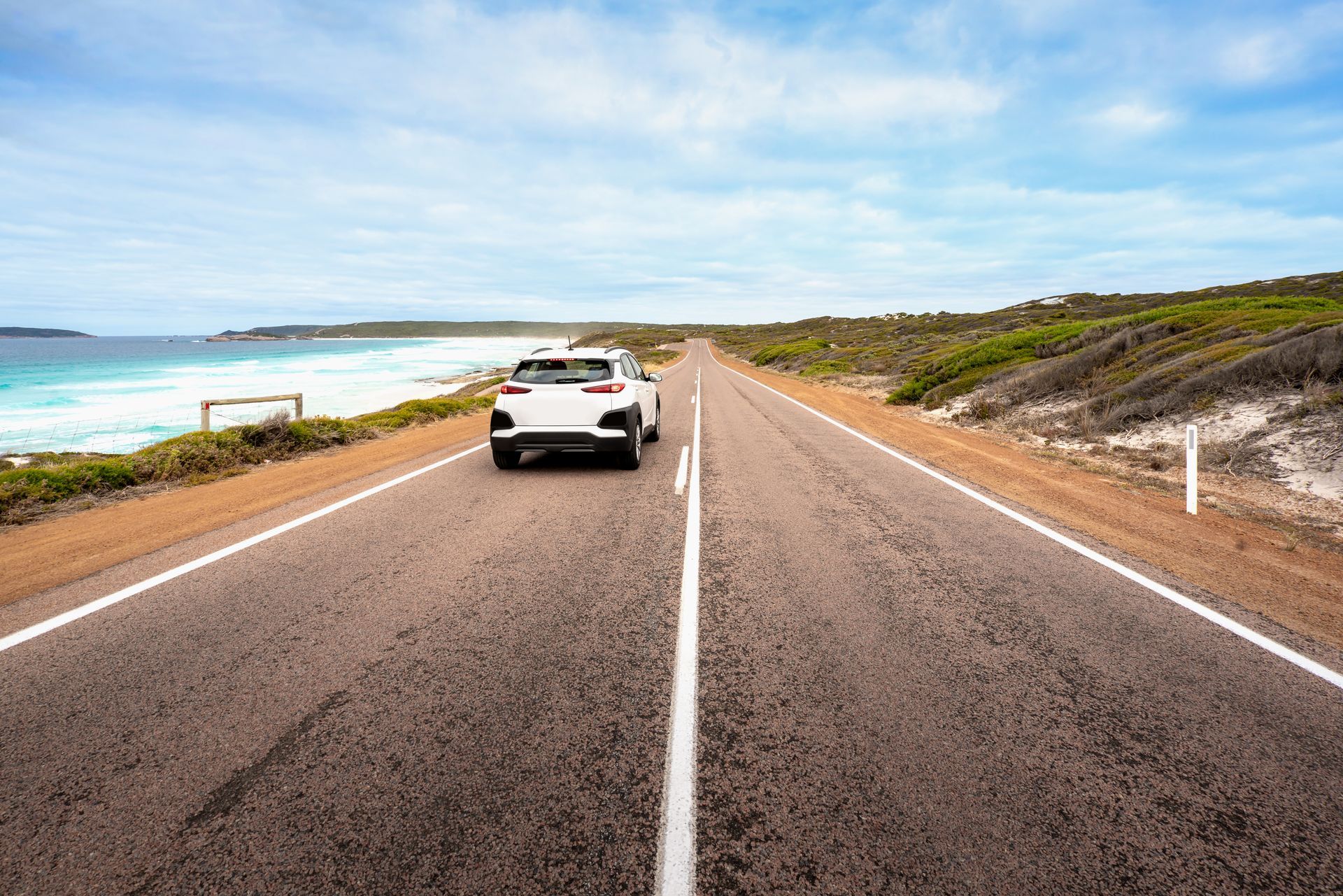White car driving on a coastal road under a cloudy sky