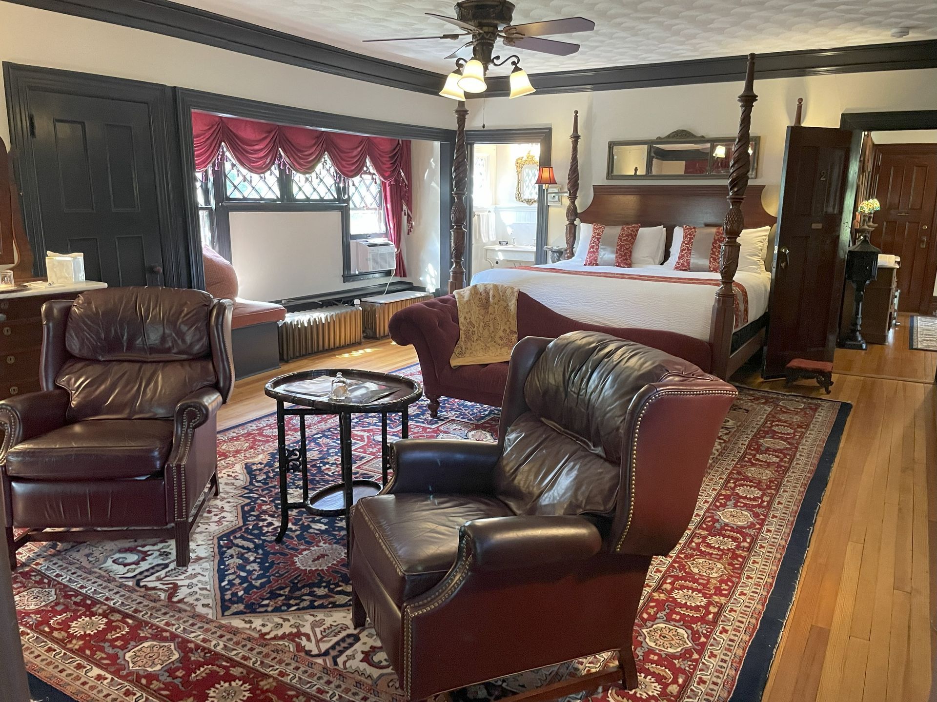 A luxurious bedroom with leather chairs, a chaise lounge, and a four-poster bed, all on a Persian rug.