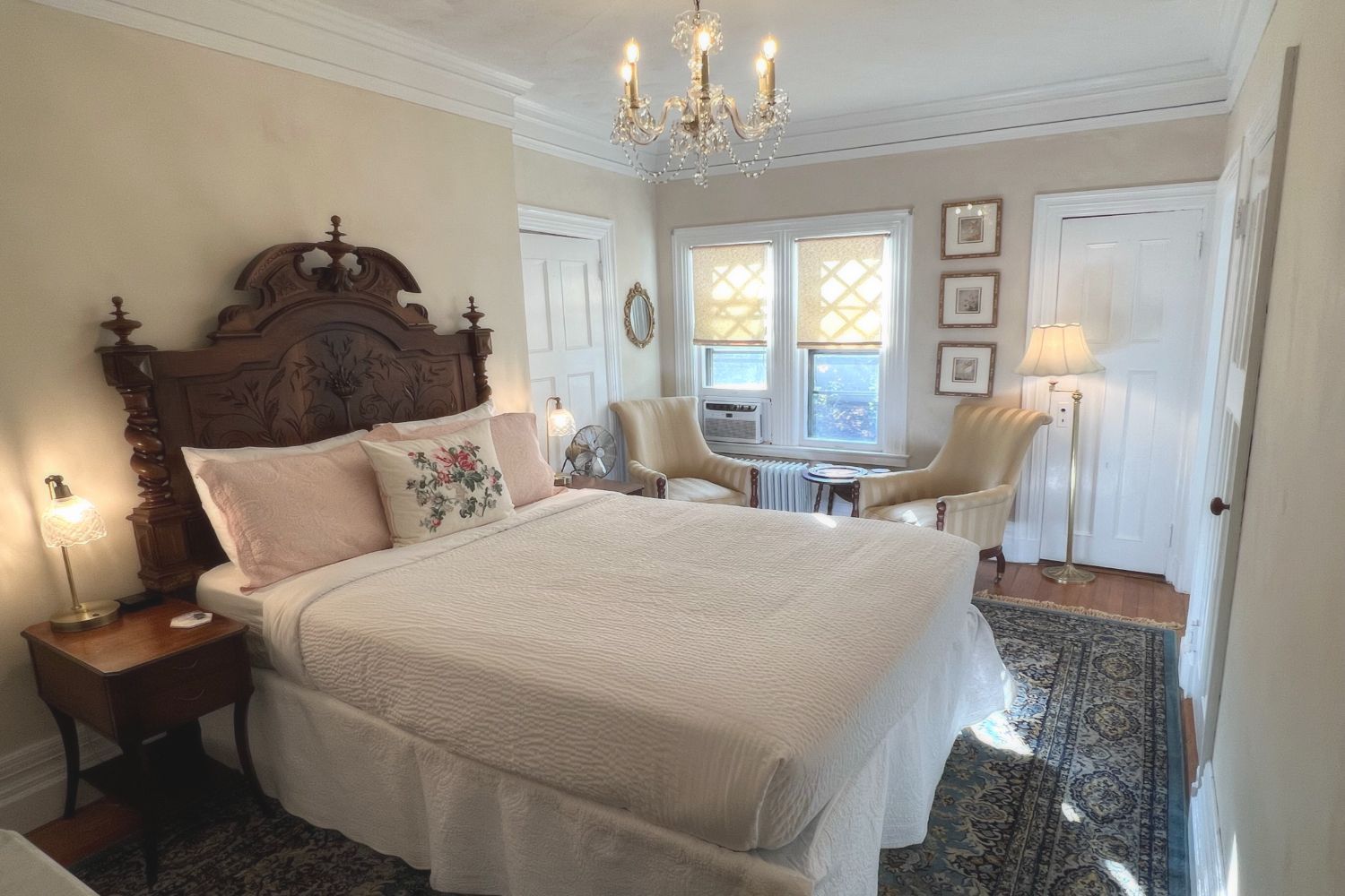 A bedroom at a New England Country Inn with a vintage French handcarved queen size bed, chairs and a chandelier.