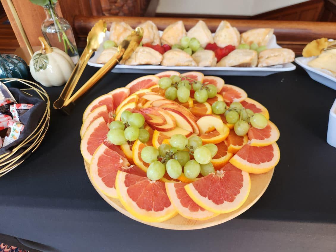 Fruit platter with grapefruit, oranges, green grapes, and apple slices, with other appetizers on a table.
