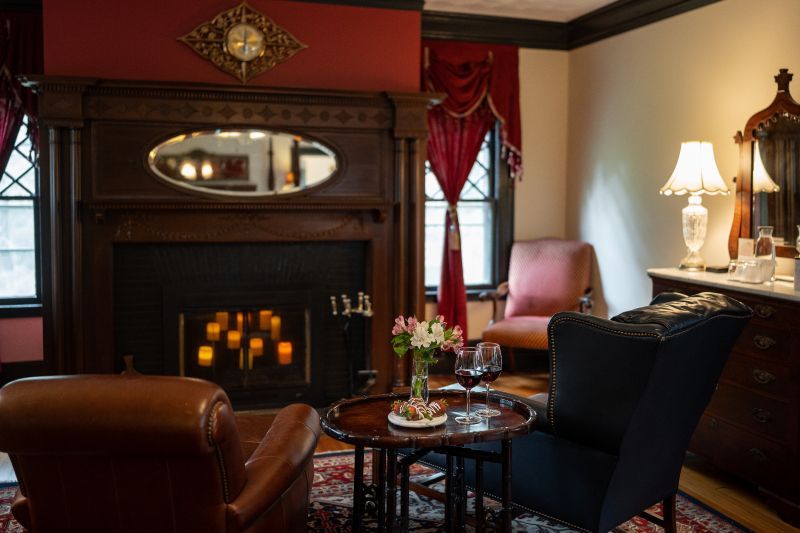 A sitting area at a New England Country Inn in a Master Bedroom with a fireplace, chairs, table with wine, and lamps.