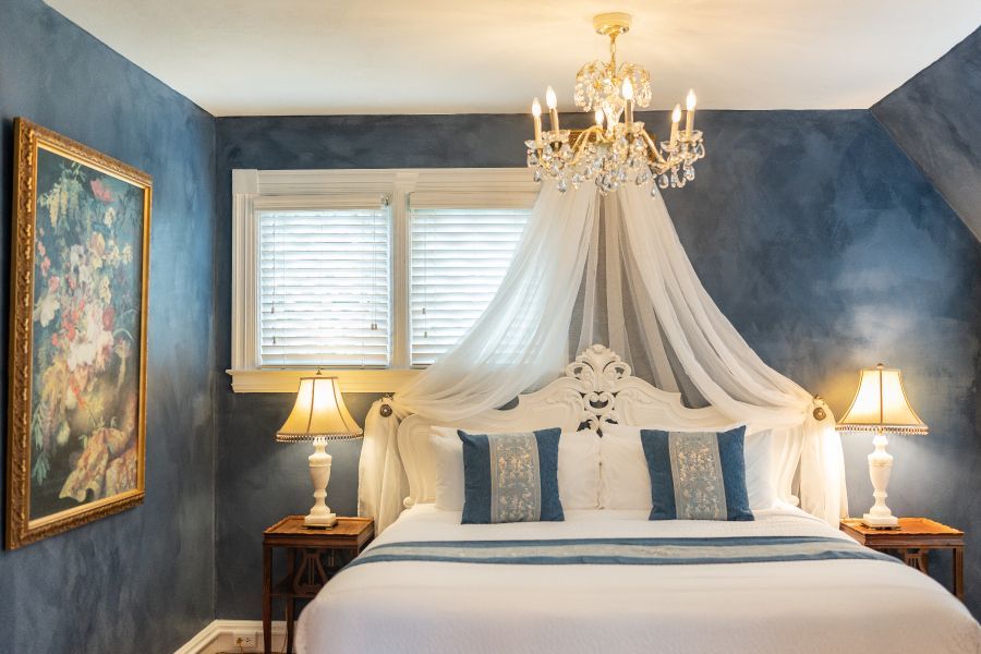 A romantic bedroom at a New England Country Inn with a bed , lamps , and a chandelier.